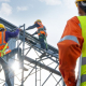 A man in a hi-vis jacket observes two construction workers on a building frame