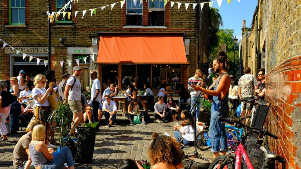 A crowd watches a street musician on a summer's day at Columbia Road Flower Market, London, UK