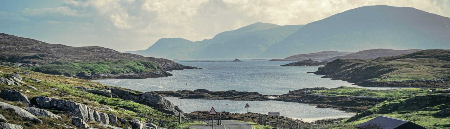 A bay surrounded by low, rocky ground with steep hills in the background, in the Western Isles, Scotland