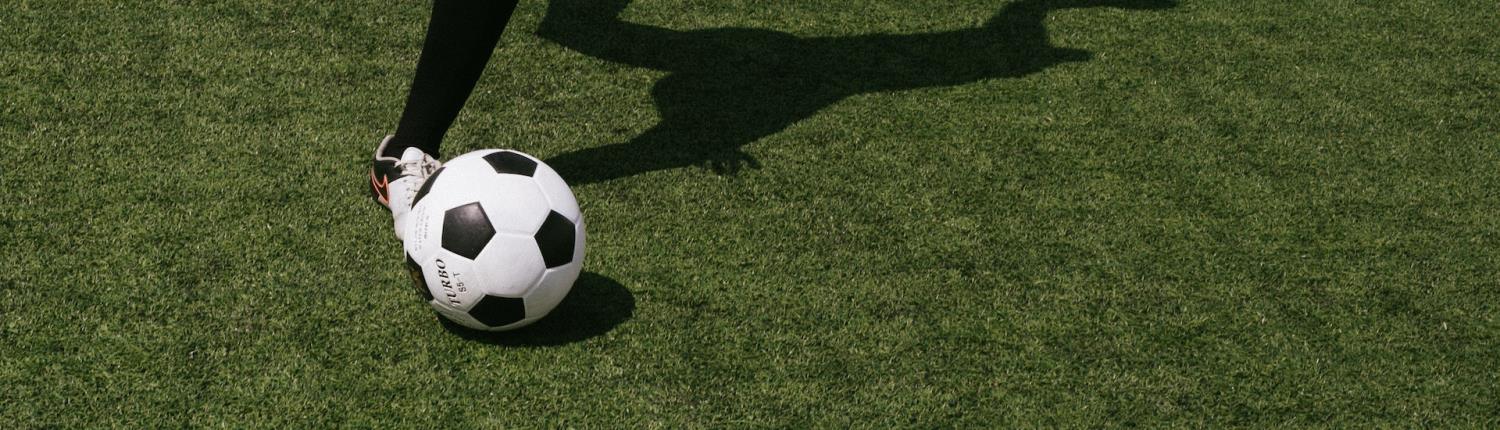 A football being kicked on a grass pitch