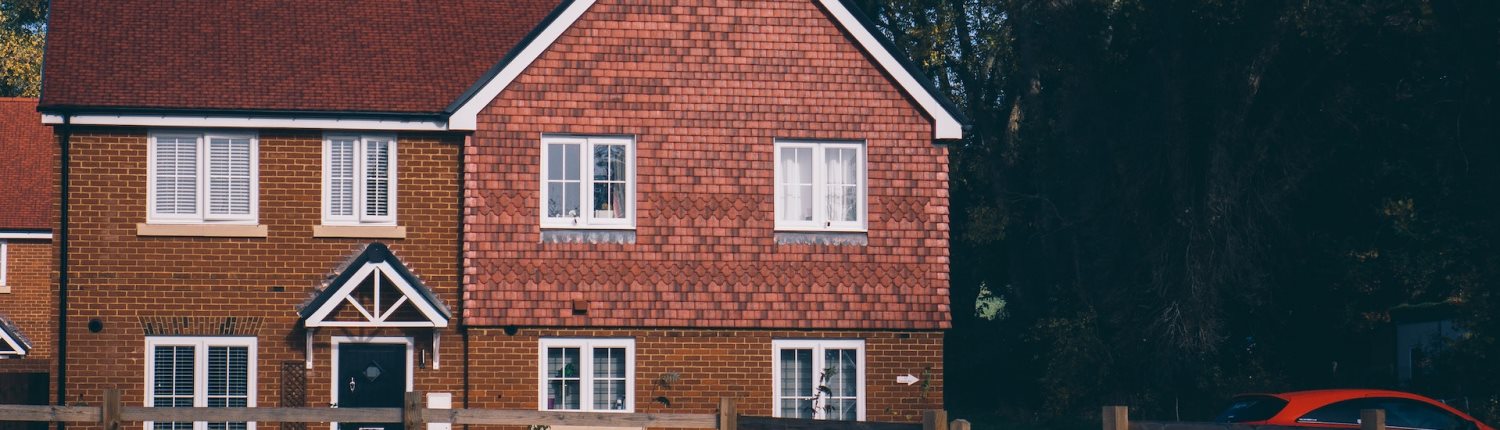 A red brick house with a tiled roof, white windowframes and a black door