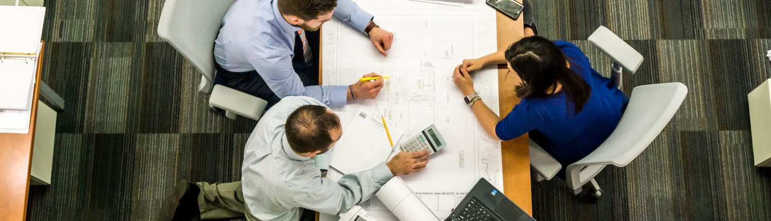 A top-down view of workers at a desk with a large schematic