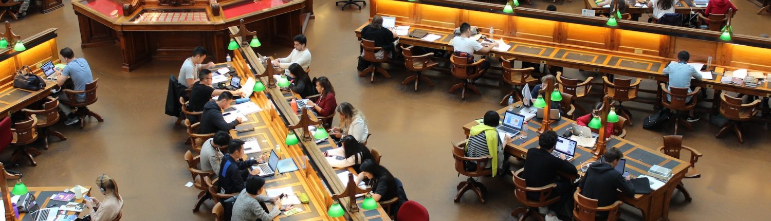 Students reading and working at laptops while seated at long desks in a university library