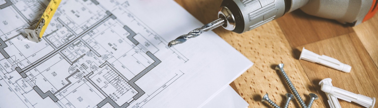 A close-up of part of a tabletop with an architectural schematic, spirit level, electric drill, screws and wall plugs